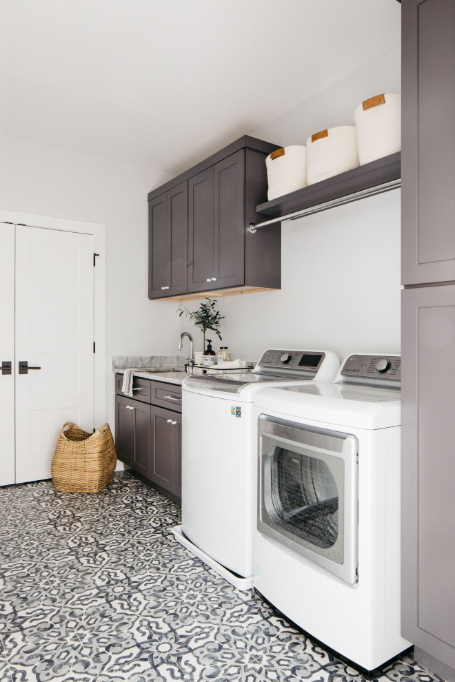 Photo of a large modern single-wall utility room in Chicago with an undermount sink, shaker cabinets, brown cabinets, white walls, a side-by-side washer and dryer, multi-coloured floor and grey benchtop.