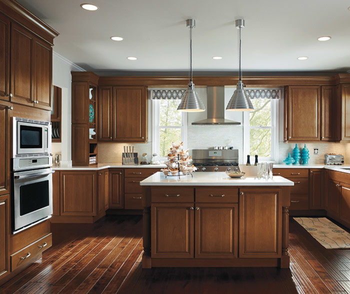 Design ideas for a mid-sized traditional u-shaped separate kitchen in Detroit with raised-panel cabinets, dark wood cabinets, solid surface benchtops, beige splashback, stainless steel appliances, dark hardwood floors, with island, brown floor and white benchtop.