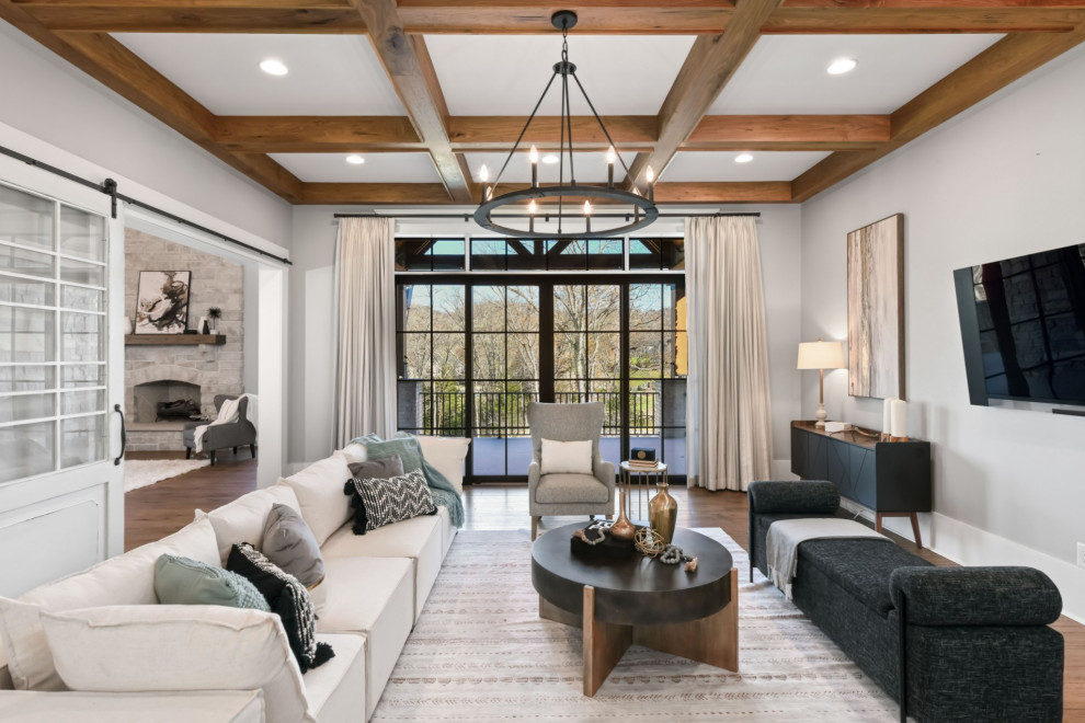 Example of a large transitional open concept medium tone wood floor, brown floor and exposed beam living room design in Nashville with gray walls, a standard fireplace, a stone fireplace and a media wall