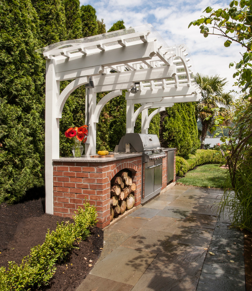 This is an example of a small traditional backyard patio in Seattle with an outdoor kitchen, natural stone pavers and a pergola.