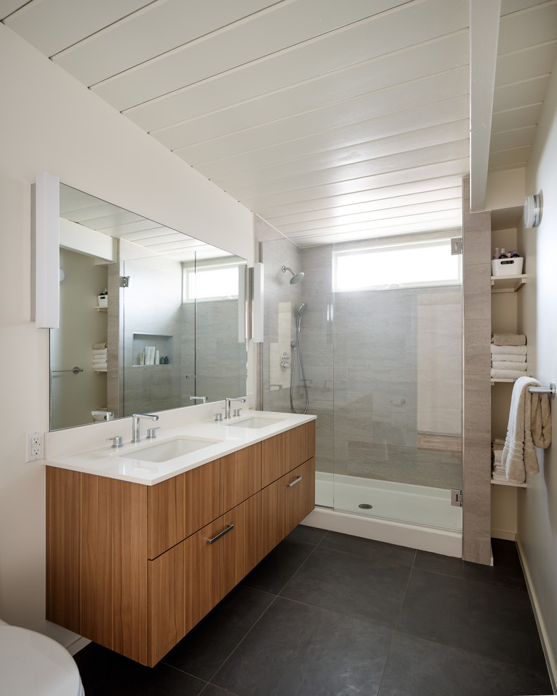 This is an example of a mid-sized midcentury master bathroom in Denver with flat-panel cabinets, medium wood cabinets, an alcove shower, a one-piece toilet, gray tile, porcelain tile, white walls, porcelain floors, an undermount sink and engineered quartz benchtops.