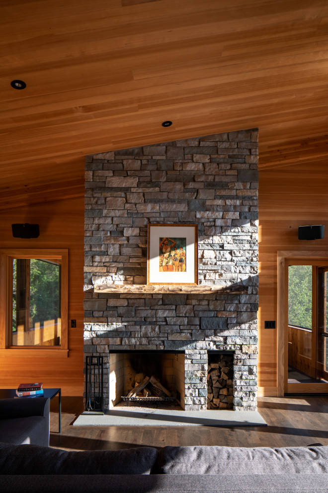 Cette image montre une petite salle de séjour en bois ouverte avec un mur marron, parquet foncé, une cheminée double-face, un manteau de cheminée en pierre, aucun téléviseur, un sol marron et un plafond en bois.