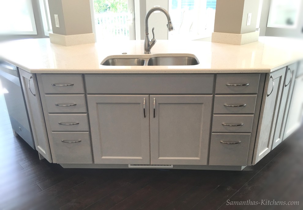 Mid-sized transitional l-shaped dark wood floor home design photo with an undermount sink, recessed-panel cabinets, gray cabinets, quartz countertops, gray backsplash, ceramic backsplash, stainless steel appliances and an island