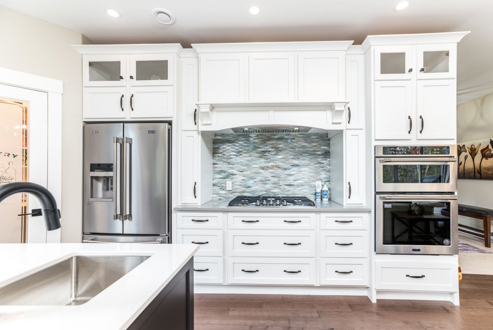 Mid-sized transitional medium tone wood floor and brown floor open concept kitchen photo with an undermount sink, shaker cabinets, white cabinets, granite countertops, gray backsplash, mosaic tile backsplash, stainless steel appliances, an island and gray countertops
