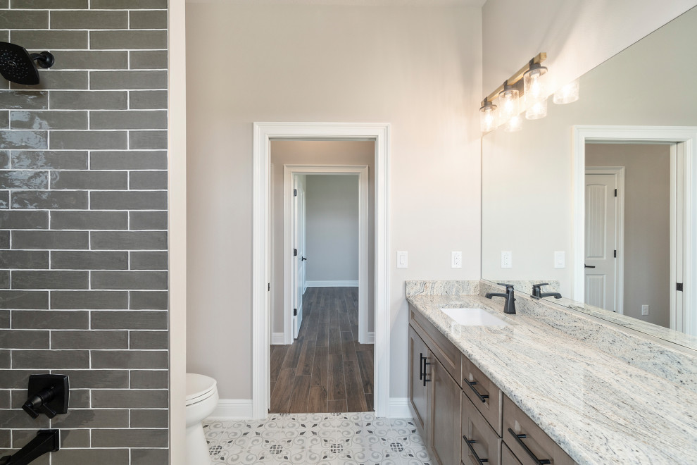 Design ideas for a mid-sized traditional bathroom in Other with shaker cabinets, light wood cabinets, an alcove tub, a shower/bathtub combo, gray tile, subway tile, grey walls, porcelain floors, solid surface benchtops, multi-coloured floor, a double vanity and a built-in vanity.