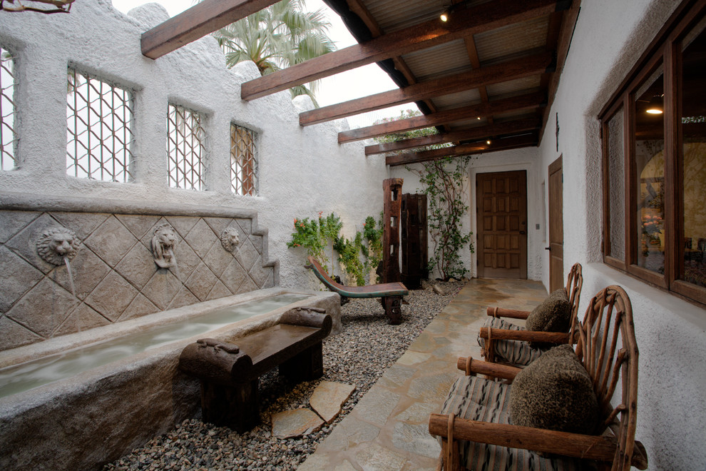 This is an example of an asian patio in Other with a water feature, natural stone pavers and a roof extension.