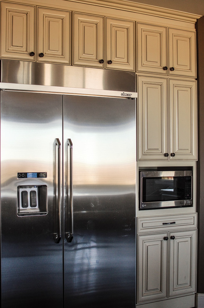 Example of a mid-sized transitional l-shaped dark wood floor and brown floor open concept kitchen design in Denver with a farmhouse sink, raised-panel cabinets, white cabinets, granite countertops, gray backsplash, porcelain backsplash, stainless steel appliances and an island