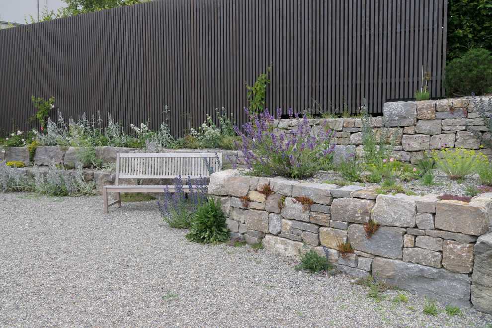 Mediterranean sloped full sun xeriscape in Stuttgart with with raised garden bed and natural stone pavers for summer.