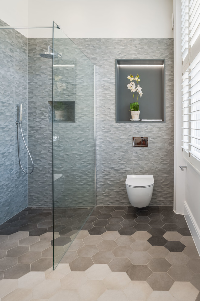 Design ideas for a mid-sized contemporary master wet room bathroom in London with flat-panel cabinets, white cabinets, a wall-mount toilet, gray tile, ceramic tile, grey walls, porcelain floors, a console sink and glass benchtops.