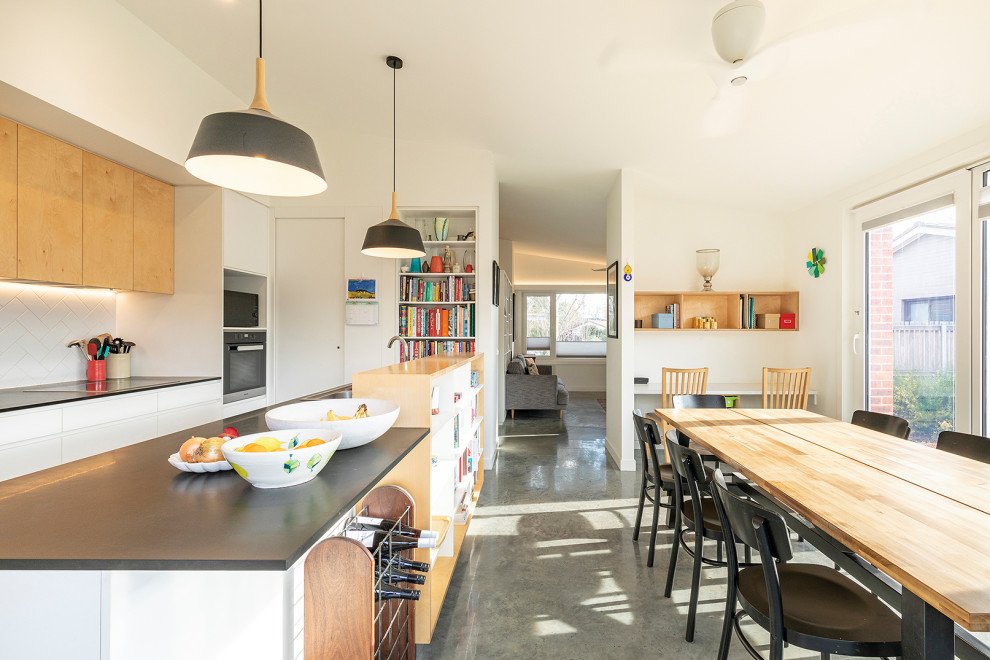 Small scandinavian galley open plan kitchen in Canberra - Queanbeyan with a double-bowl sink, flat-panel cabinets, white splashback, ceramic splashback, stainless steel appliances, concrete floors, with island, grey floor and black benchtop.
