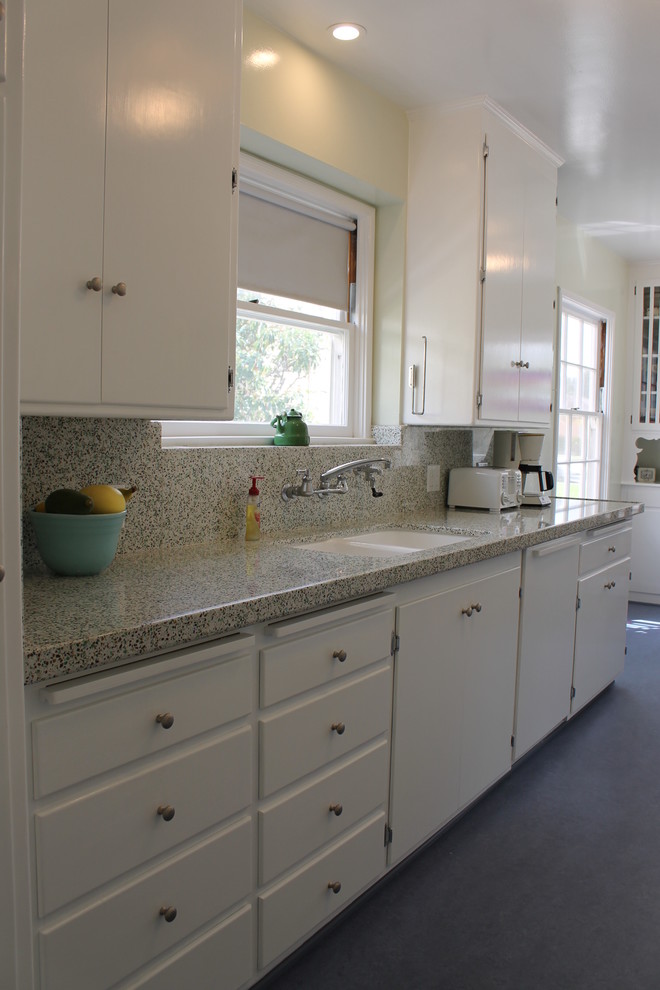 This is an example of a mid-sized tropical galley separate kitchen in Los Angeles with a double-bowl sink, white cabinets, quartz benchtops, multi-coloured splashback, white appliances, linoleum floors, no island and flat-panel cabinets.