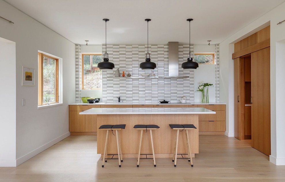 Contemporary galley open plan kitchen in San Francisco with an undermount sink, flat-panel cabinets, light wood cabinets, grey splashback, panelled appliances, light hardwood floors, with island, white benchtop, matchstick tile splashback and beige floor.