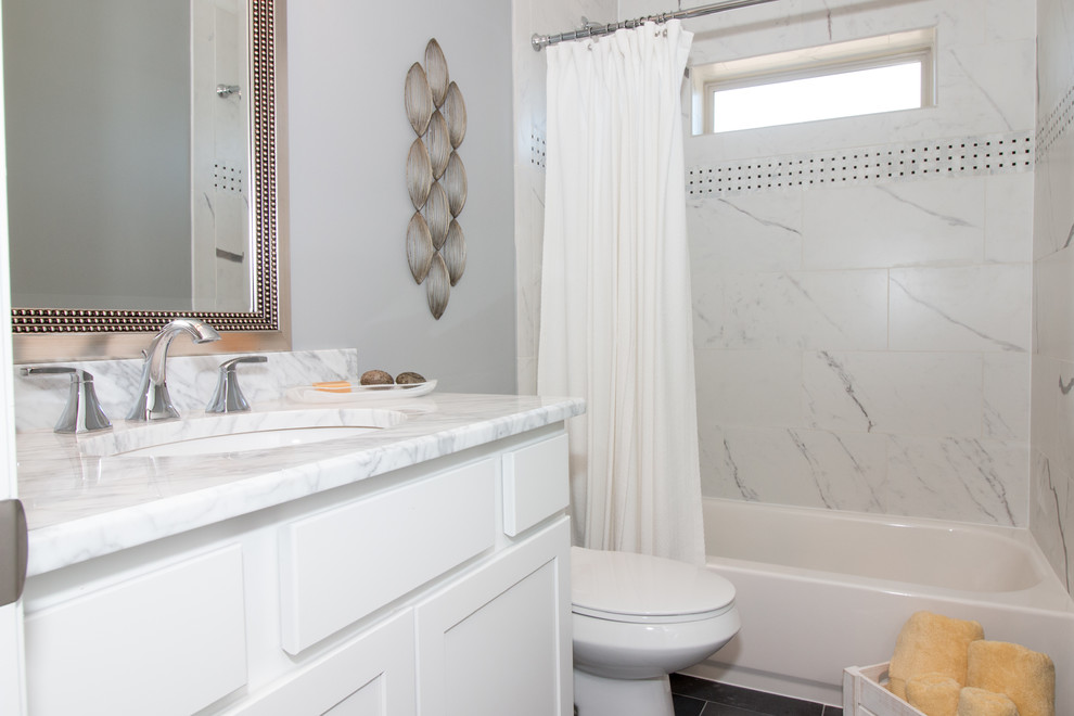 Photo of a mid-sized transitional kids bathroom in Chicago with shaker cabinets, white cabinets, a corner tub, a shower/bathtub combo, a two-piece toilet, grey walls, an undermount sink, marble benchtops, gray tile, porcelain tile, porcelain floors and grey floor.