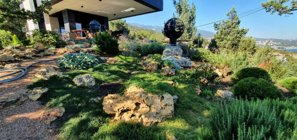 На фото: большой солнечный, летний засухоустойчивый сад на склоне в средиземноморском стиле с камнем в ландшафтном дизайне, хорошей освещенностью и с каменным забором с