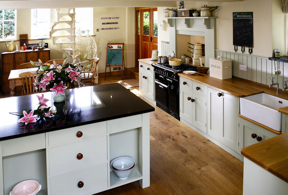 Inspiration for a medium sized classic kitchen/diner in Kent with a belfast sink, shaker cabinets, white cabinets, wood worktops, black appliances, medium hardwood flooring and an island.