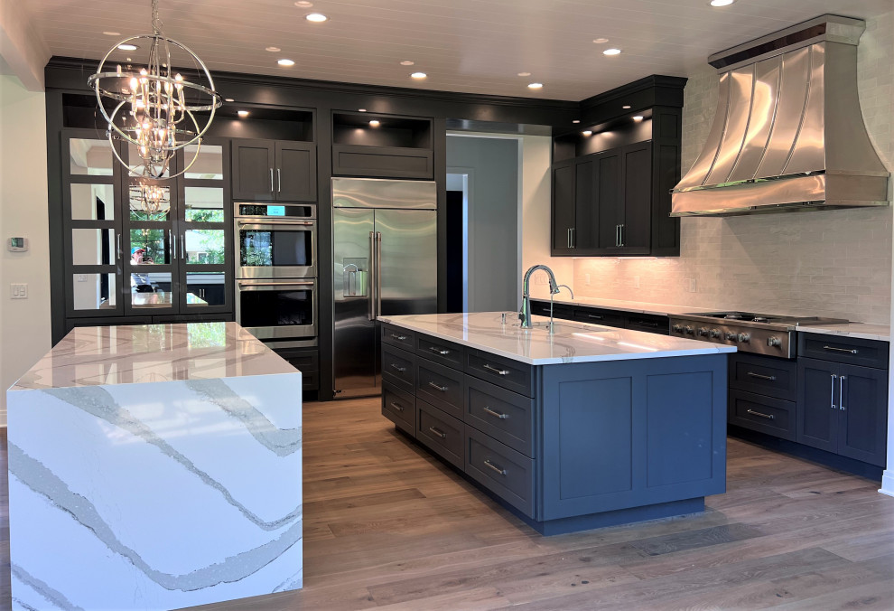 Large transitional kitchen photo with an undermount sink, shaker cabinets, gray cabinets, quartz countertops, white backsplash, stainless steel appliances, two islands and white countertops