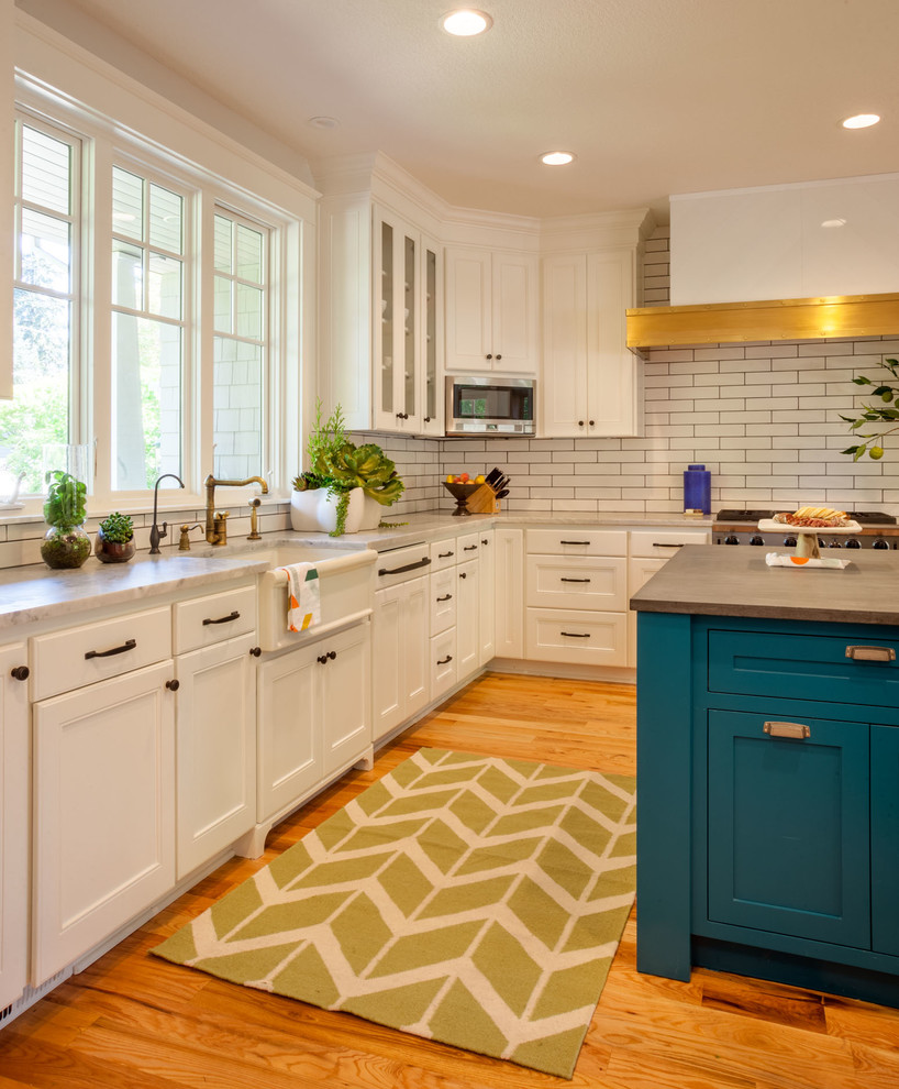 Enclosed kitchen - mid-sized transitional u-shaped medium tone wood floor enclosed kitchen idea in Portland with an island, a farmhouse sink, recessed-panel cabinets, white cabinets, marble countertops, white backsplash, subway tile backsplash and stainless steel appliances