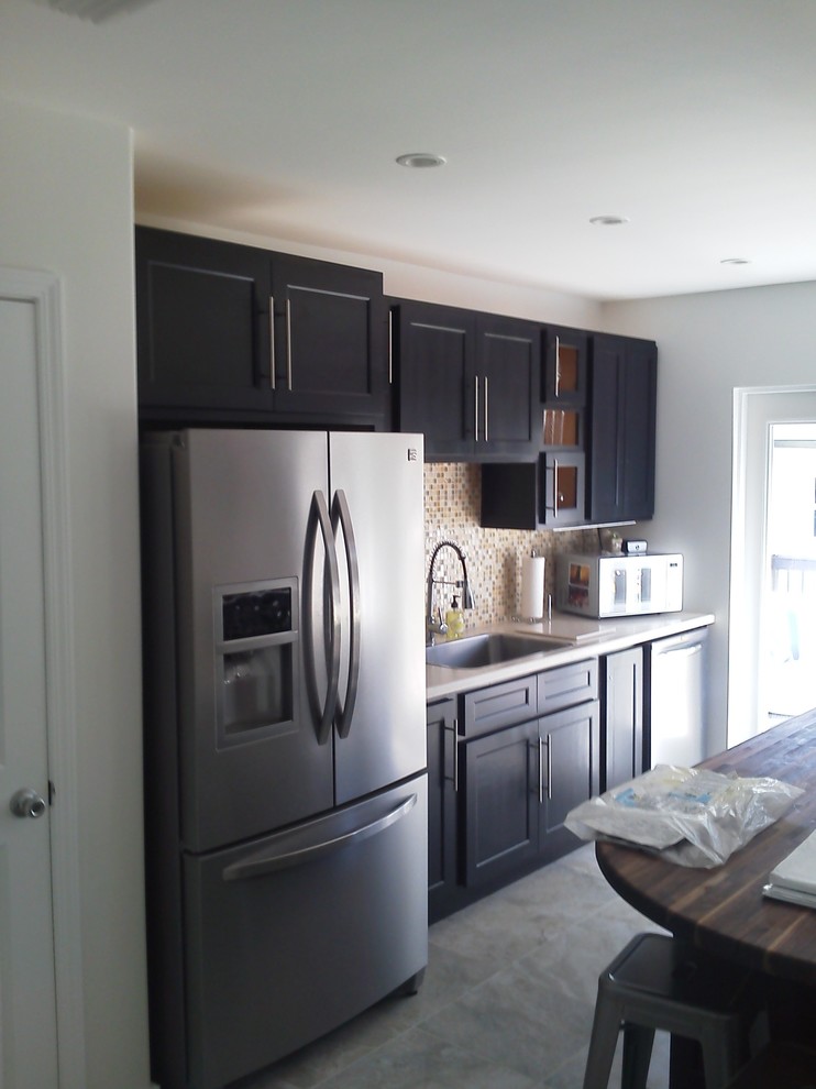 Example of a mid-sized transitional galley porcelain tile and gray floor eat-in kitchen design in Miami with a double-bowl sink, shaker cabinets, black cabinets, solid surface countertops, multicolored backsplash, mosaic tile backsplash, stainless steel appliances and an island