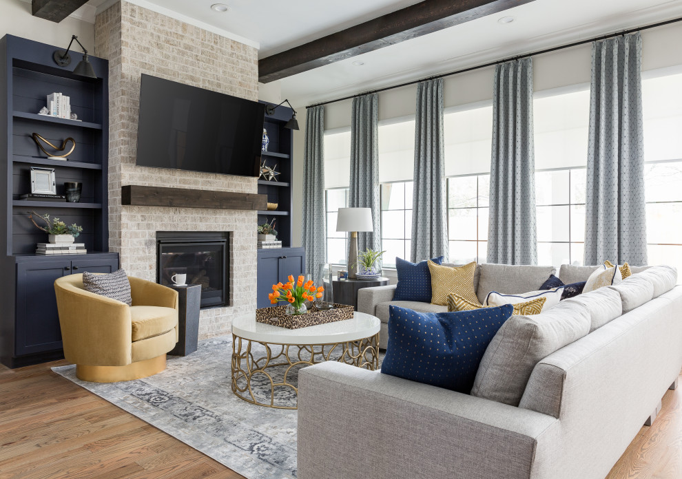 Design ideas for a transitional open concept living room in Houston with white walls, medium hardwood floors, a standard fireplace, a brick fireplace surround, a wall-mounted tv, brown floor and exposed beam.