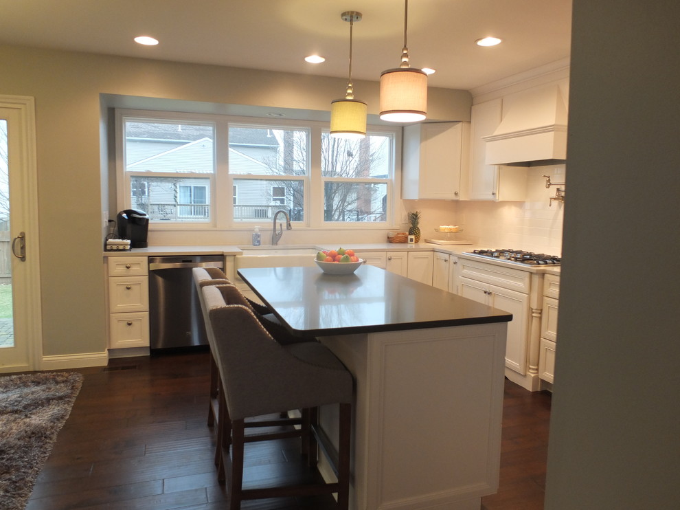 Photo of a mid-sized transitional u-shaped eat-in kitchen in Columbus with with island, flat-panel cabinets, white cabinets, quartz benchtops, white splashback, ceramic splashback, stainless steel appliances, a farmhouse sink and dark hardwood floors.
