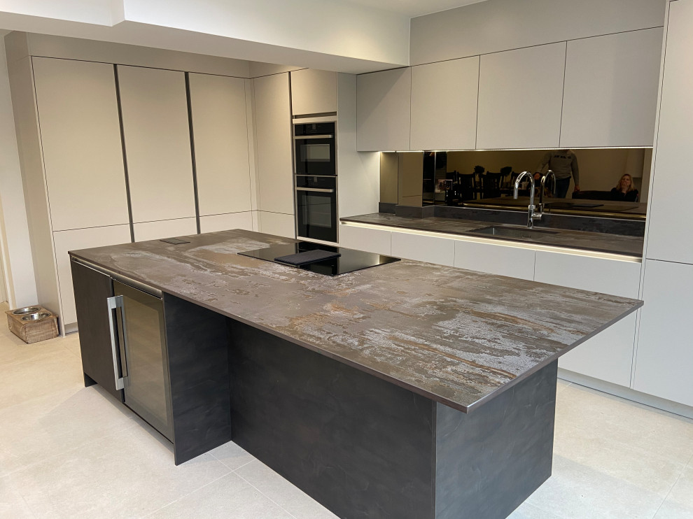 Example of a large trendy galley porcelain tile and white floor kitchen design in London with quartzite countertops, mirror backsplash, recessed-panel cabinets, gray cabinets and an island