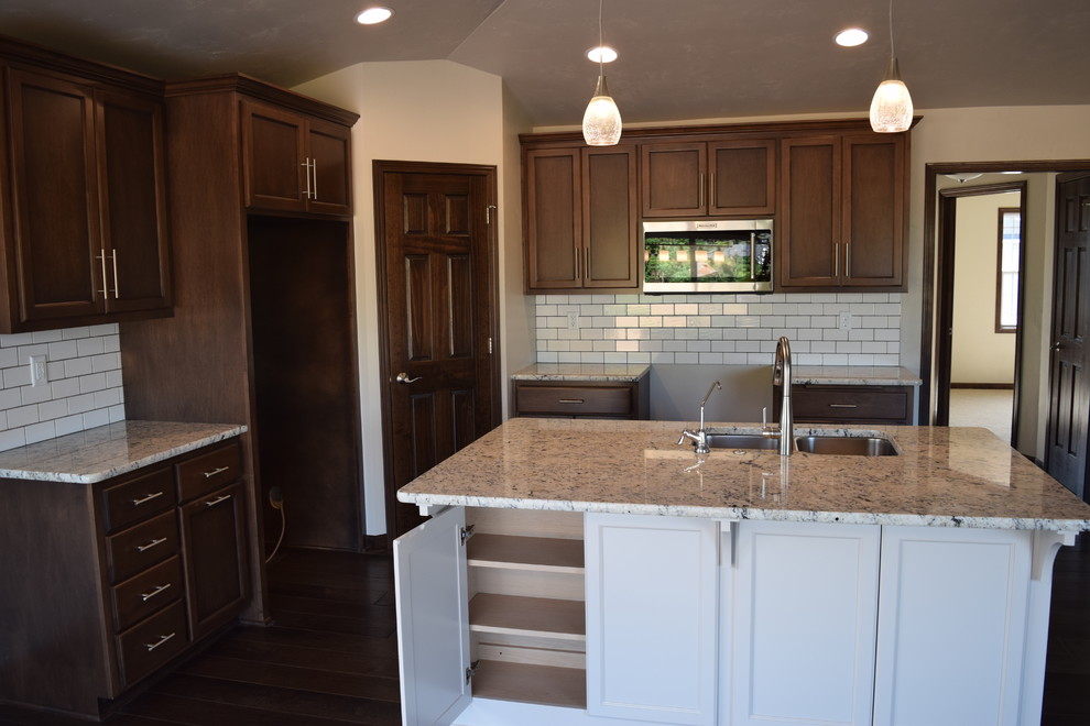 Inspiration for a large medium tone wood floor and brown floor open concept kitchen remodel with an undermount sink, recessed-panel cabinets, medium tone wood cabinets, granite countertops, white backsplash, ceramic backsplash, stainless steel appliances and an island