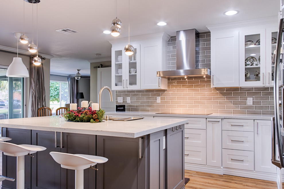 Mid-sized transitional l-shaped open plan kitchen in Phoenix with an undermount sink, shaker cabinets, white cabinets, wood benchtops, grey splashback, subway tile splashback, stainless steel appliances, light hardwood floors and with island.