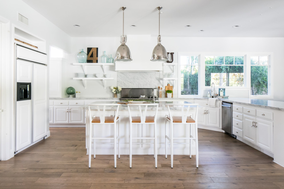 Beach style u-shaped kitchen in Orange County with raised-panel cabinets, white cabinets, stainless steel appliances, medium hardwood floors, with island, brown floor and grey benchtop.