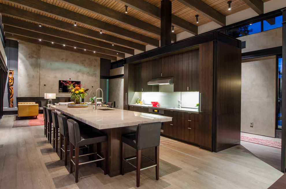 This is an example of a large contemporary galley open plan kitchen in Seattle with flat-panel cabinets, dark wood cabinets, with island, an undermount sink, white splashback, onyx benchtops, glass sheet splashback, stainless steel appliances, light hardwood floors and beige floor.