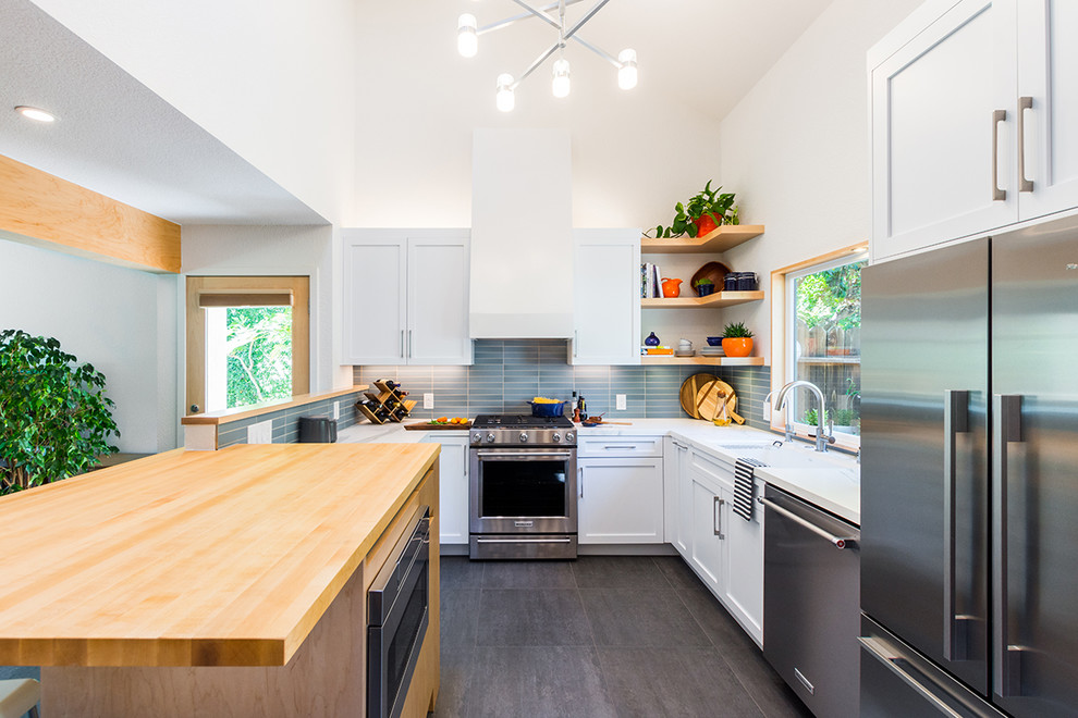 This is an example of a mid-sized transitional u-shaped open plan kitchen in Sacramento with an undermount sink, shaker cabinets, white cabinets, quartzite benchtops, blue splashback, glass tile splashback, stainless steel appliances, porcelain floors, with island, grey floor and white benchtop.