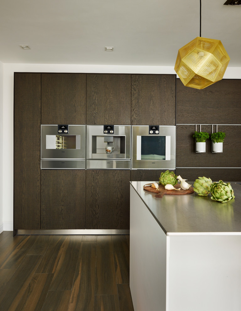 Design ideas for a large contemporary galley separate kitchen in Devon with an integrated sink, flat-panel cabinets, dark wood cabinets, stainless steel benchtops, white splashback, subway tile splashback, panelled appliances, porcelain floors and with island.