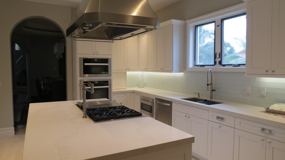 Large transitional l-shaped light wood floor and beige floor enclosed kitchen photo with a double-bowl sink, shaker cabinets, white cabinets, marble countertops, blue backsplash, glass tile backsplash, stainless steel appliances and an island