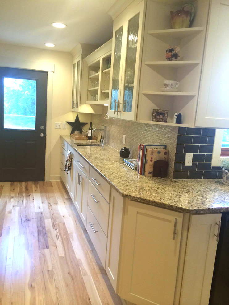 Inspiration for a large transitional l-shaped eat-in kitchen in Milwaukee with an undermount sink, shaker cabinets, white cabinets, granite benchtops, beige splashback, ceramic splashback, stainless steel appliances, light hardwood floors and with island.