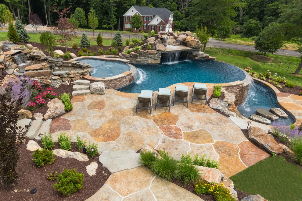 Expansive country backyard custom-shaped infinity pool with a water feature and natural stone pavers.
