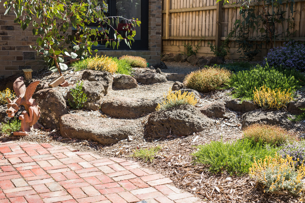 Small midcentury courtyard full sun xeriscape in Melbourne with brick pavers.