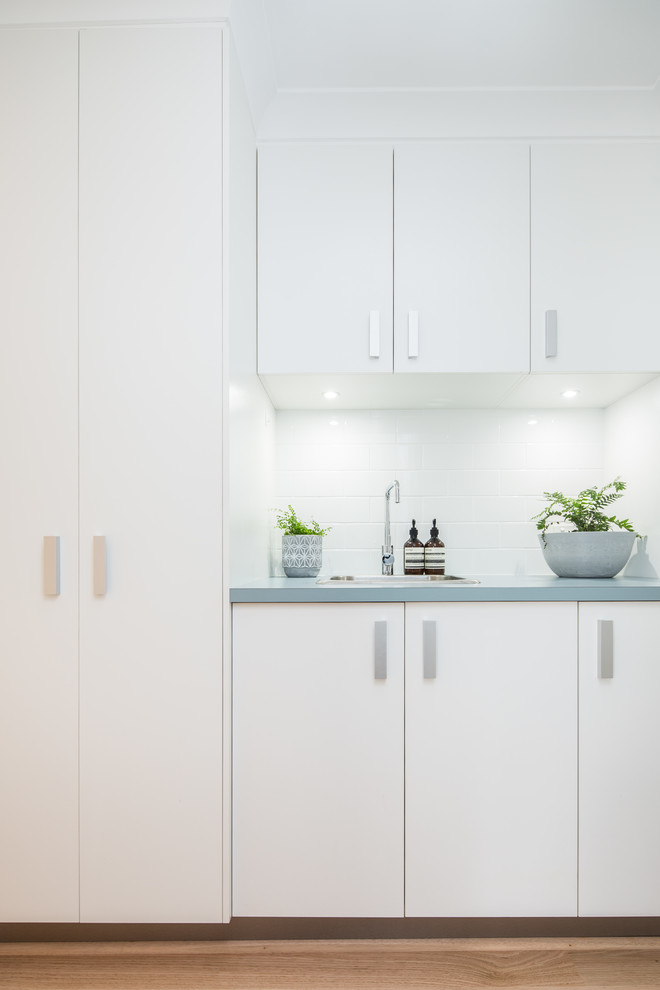 Small traditional single-wall dedicated laundry room in Canberra - Queanbeyan with a drop-in sink, white cabinets, laminate benchtops, white walls, light hardwood floors, an integrated washer and dryer, beige floor and turquoise benchtop.