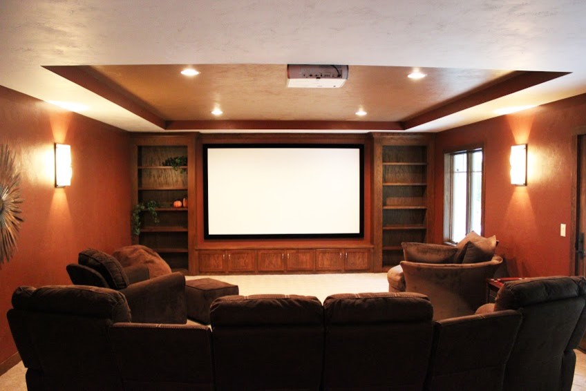 Large enclosed carpeted home theater photo with multicolored walls and a projector screen