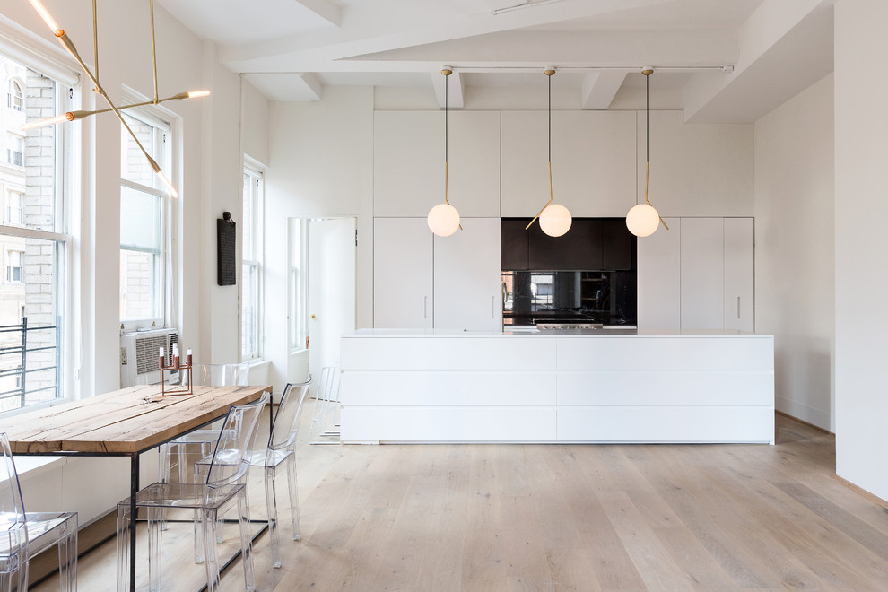 Design ideas for a mid-sized scandinavian galley eat-in kitchen in New York with flat-panel cabinets, white cabinets, light hardwood floors, with island, solid surface benchtops, black splashback, stainless steel appliances and glass sheet splashback.