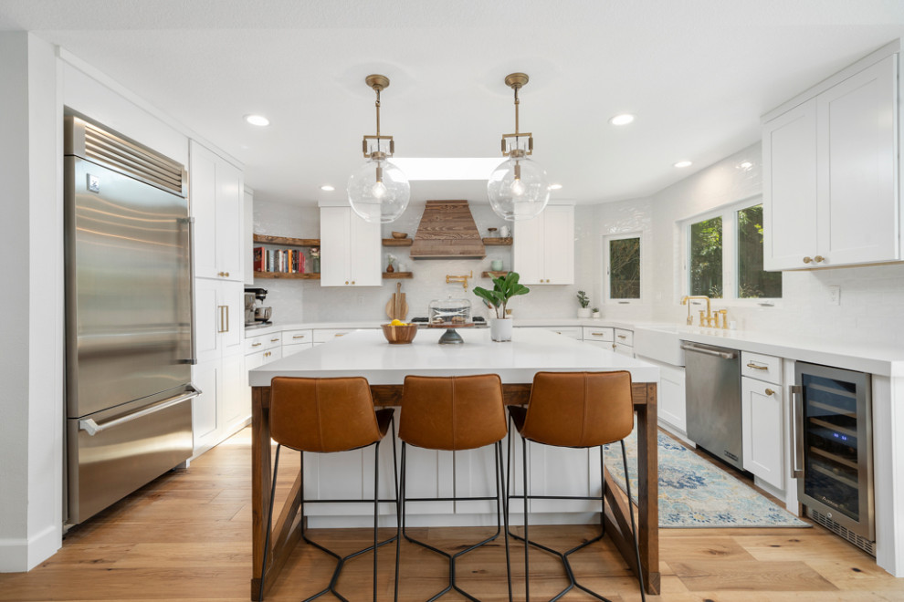 Inspiration for a mid-sized country open plan kitchen in Orange County with a farmhouse sink, shaker cabinets, white cabinets, quartz benchtops, white splashback, porcelain splashback, coloured appliances, light hardwood floors, with island, brown floor and white benchtop.