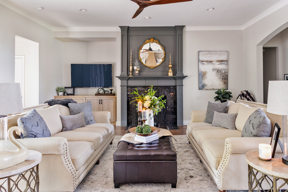 Cette image montre un grand salon traditionnel ouvert avec un mur gris, un sol en bois brun, une cheminée standard, un manteau de cheminée en pierre, un téléviseur fixé au mur et un sol marron.