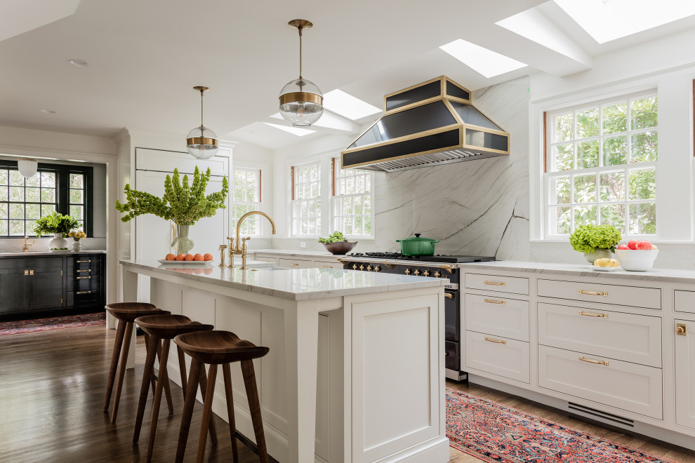Photo of an expansive transitional l-shaped kitchen in Boston with a farmhouse sink, shaker cabinets, white cabinets, grey splashback, panelled appliances, medium hardwood floors, with island, brown floor and grey benchtop.