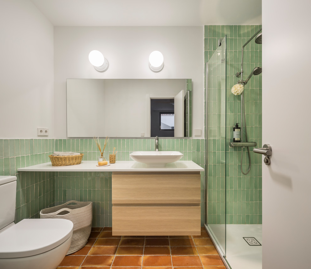 Пример оригинального дизайна: маленькая ванная комната в средиземноморском стиле с терракотовой плиткой, белыми стенами, полом из терракотовой плитки, столешницей из искусственного кварца, коричневым полом, светлыми деревянными фасадами, зеленой плиткой, настольной раковиной, белой столешницей и подвесной тумбой для на участке и в саду