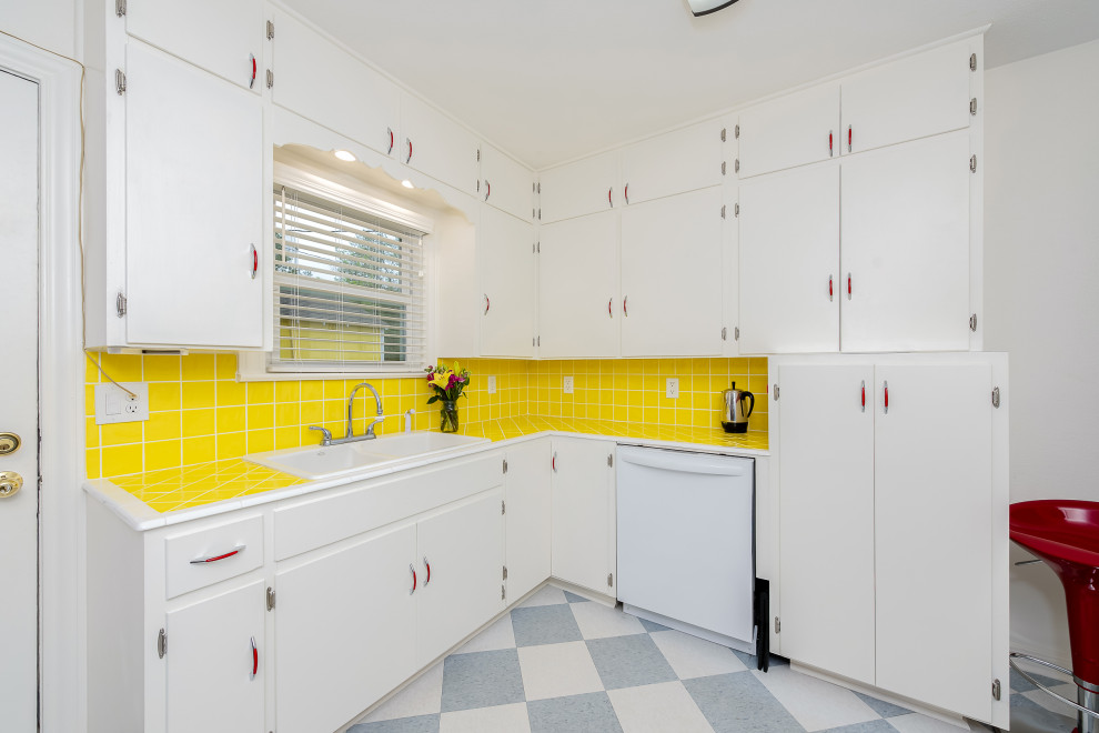 オースティンにあるトラディショナルスタイルのおしゃれなキッチン (ダブルシンク、フラットパネル扉のキャビネット、白いキャビネット、タイルカウンター、黄色いキッチンパネル、セラミックタイルのキッチンパネル、白い調理設備、アイランドなし、青い床、黄色いキッチンカウンター) の写真