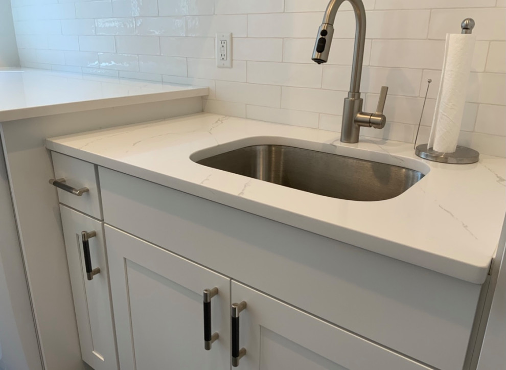Inspiration for a mid-sized transitional galley dedicated laundry room in New York with an undermount sink, shaker cabinets, white cabinets, quartz benchtops, white splashback, ceramic splashback, grey walls, ceramic floors, an integrated washer and dryer, grey floor and white benchtop.