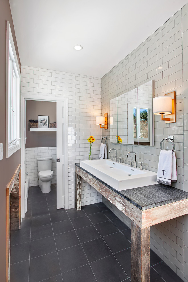 Photo of a mid-sized country master bathroom in New York with a trough sink, distressed cabinets, soapstone benchtops, white tile, subway tile, grey walls, porcelain floors and a two-piece toilet.