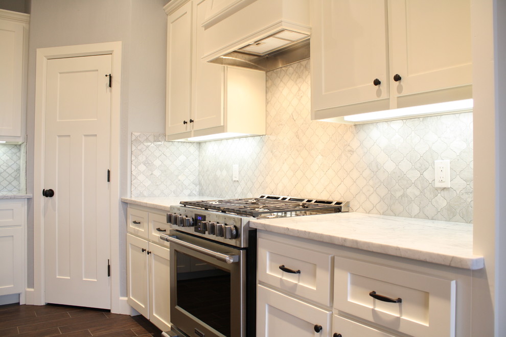 This is an example of a mid-sized arts and crafts l-shaped open plan kitchen in Oklahoma City with an undermount sink, shaker cabinets, white cabinets, marble benchtops, white splashback, mosaic tile splashback, stainless steel appliances, ceramic floors and with island.