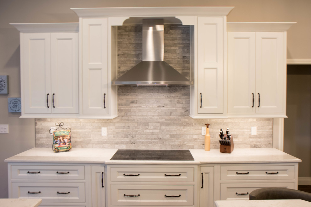Photo of a large transitional kitchen in Orlando with a farmhouse sink, recessed-panel cabinets, white cabinets, quartzite benchtops, grey splashback, marble splashback, stainless steel appliances, medium hardwood floors, with island, brown floor and white benchtop.