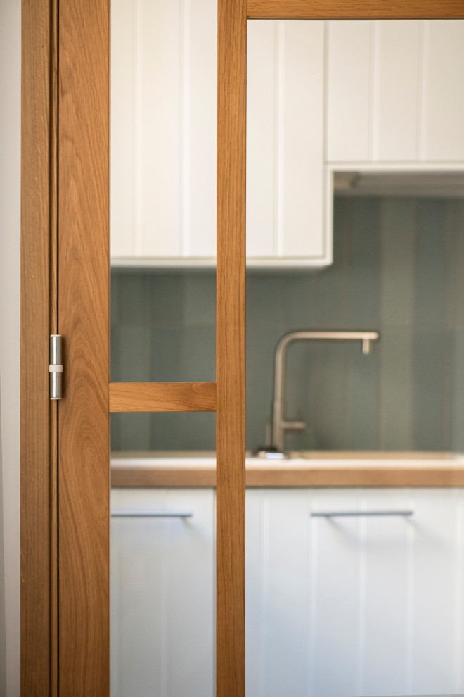 Idée de décoration pour cuisine en L avec un évier 1 bac, un placard à porte plane, des portes de placard blanches, un plan de travail en bois, une crédence bleue, une crédence en céramique, un électroménager en acier inoxydable, carreaux de ciment au sol, aucun îlot, un sol bleu et un plan de travail beige.