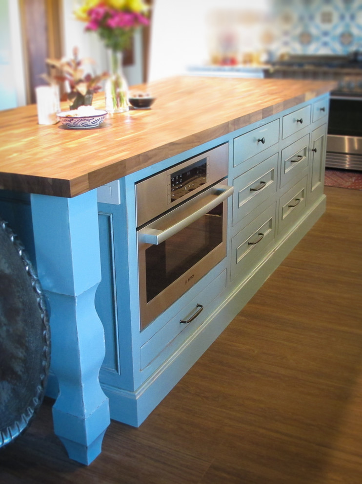 Dark wood floor kitchen photo with a farmhouse sink, beaded inset cabinets, white cabinets, multicolored backsplash, ceramic backsplash, stainless steel appliances and an island