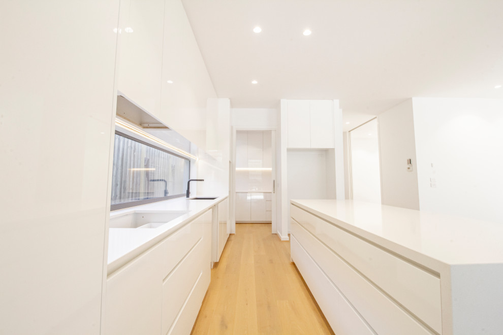 Inspiration for a large contemporary galley open plan kitchen in Melbourne with an undermount sink, recessed-panel cabinets, white cabinets, concrete benchtops, white splashback, ceramic splashback, stainless steel appliances, laminate floors, with island and white benchtop.